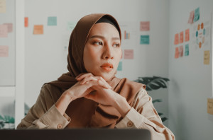 Woman at work looking to one side with serious expression, with Post-Its on the wall behind her