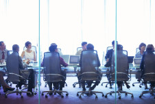 View from behind: about 10 employees sitting at a conference table looking to the right