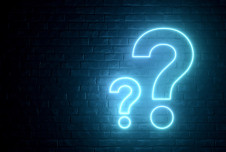 Two neon question marks against a black brick background