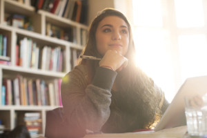 Teen girl with notebook in hand, bookshelf behind her, looking up with sun streaming in from window