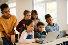Six elementary students gathered around a laptop in the classroom