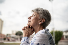 Pensive woman outdoors, looking upward with her chin in her hands