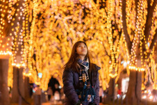 Woman outdoors looking up at vibrant holiday lights on trees