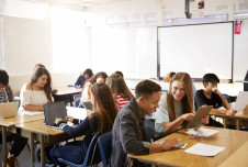 A high school classroom with students working at their desk and whiteboard in the background