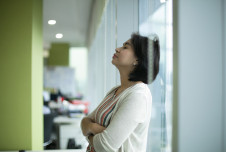 Woman at work leaning against glass wall with eyes closed
