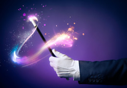 Magician’s gloved hand holding a wand with a swirl of light and glitter coming off of it