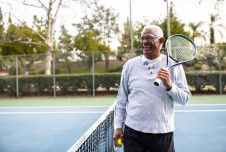 Older man smiling and holding a tennis racket on a tennis court