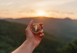 Hand holding up compass with mountains in the background
