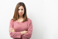 Angry woman with her arms crossed, against plain background