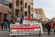 A group of protestors march with a sign that says "Stop Racist Police Terror"