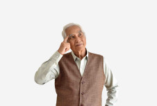 An image showing an elderly man in a vest, thoughtfully touching his temple