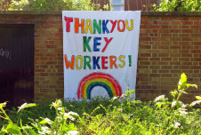 A large, hand-painted banner with the message "THANK YOU KEY WORKERS!" adorned with colorful letters and a rainbow, displayed on a brick wall surrounded by greenery.