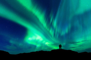 Beautiful aurora borealis with two small people on hillside