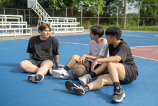 Three teen boys sitting on a basketball court talking