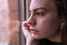 Woman looking out the window with chin in hand and tear running down her cheek