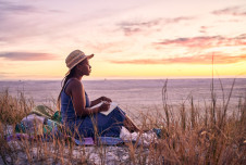 A woman sitting on a beach at sunset, writing in a notebook