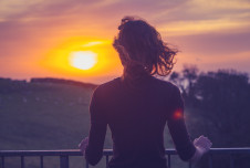A person standing on a balcony, watching the sunset over a peaceful landscape