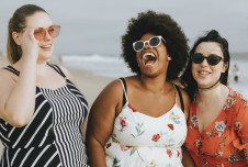Three women laughing together at the beach.