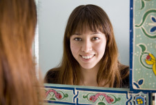 A woman with long hair is smiling at her reflection in a decorative mirror