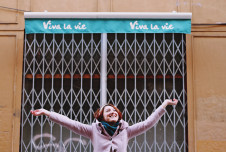 a woman standing in front of a building with her arms outstretched, smiling joyfully