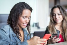 Two women are sitting together, each engrossed in their smartphones