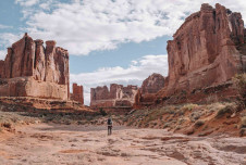 an image showing a person standing in a vast, open landscape surrounded by towering red rock formations