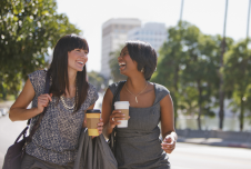 Two women carrying coffees laughing together