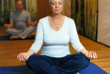 A picture of an older woman practicing yoga in a seated meditation pose on a blue mat