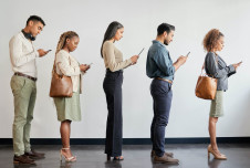 Five people standing in a line, each engrossed in their smartphones