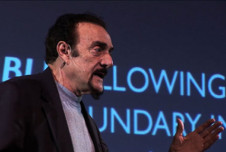 Philip Zimbardo speaking on stage, wearing a dark blazer and a light gray shirt