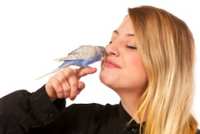 an image showing a woman with blonde hair, smiling and looking lovingly at a small bird perched on her finger